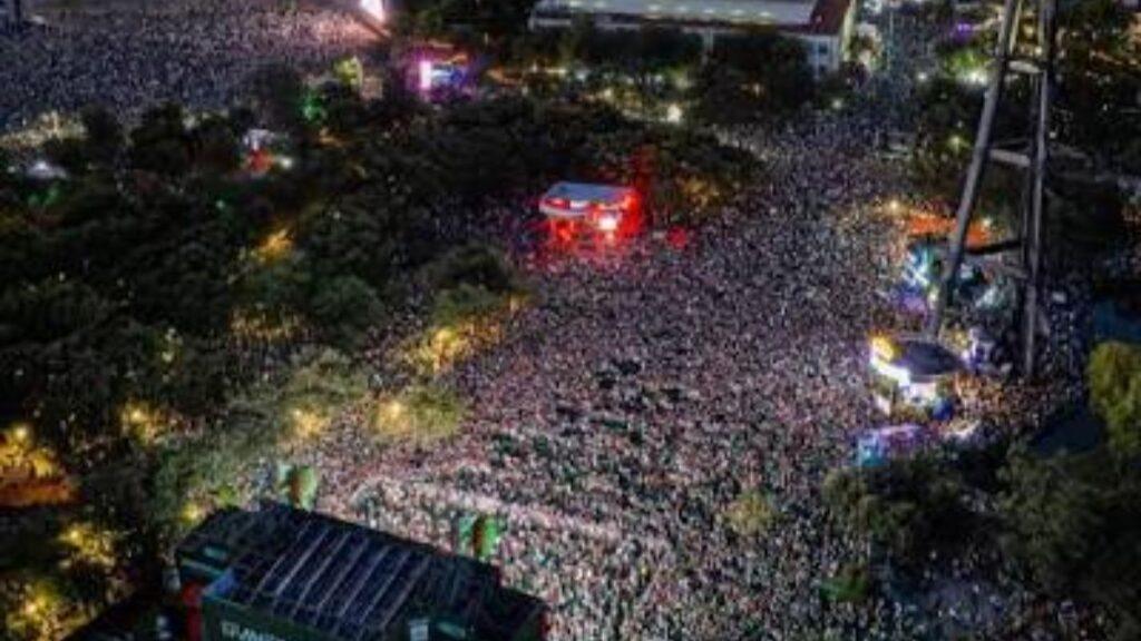 Aerial View of a Massive Nighttime Concert Crowd in a Park, with Stage Lights and a Red-lit Area Near the Center. | Ciudadano Seguros
