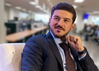 Moches-en-el-instituto-registral | Ciudadano Seguros Man in a Navy Suit and Brown Tie Sits on a White Chair in a Bright, Modern Office Lobby, Looking Thoughtful. | Ciudadano Seguros