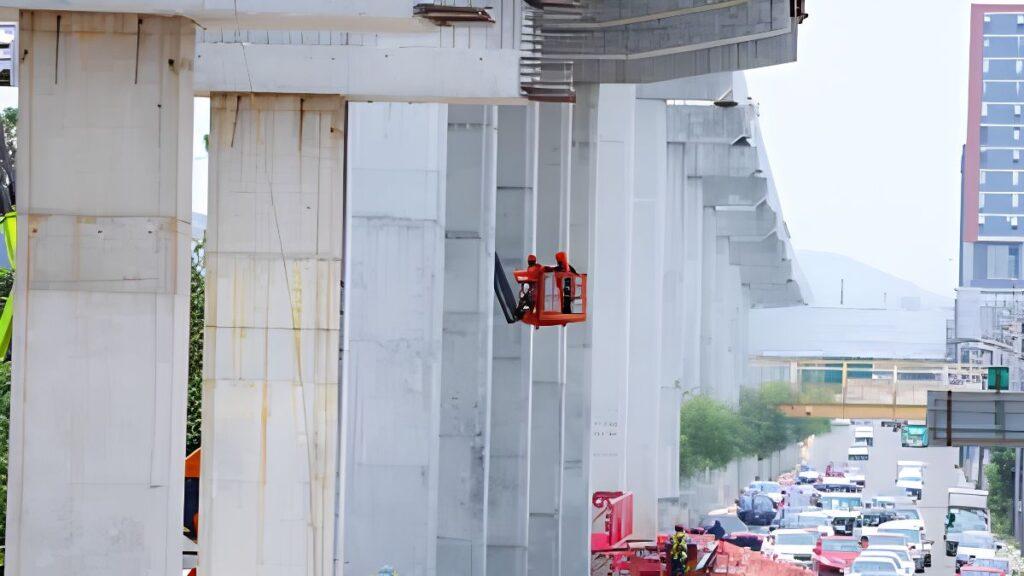Two Workers in a Red Elevated Basket on a Construction Platform Working on a Concrete Overpass Above a Busy Street Thanked by Traffic Below. | Ciudadano Seguros