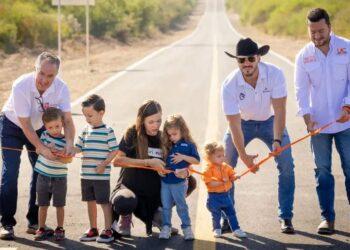 Group of Adults and Children Participate in a Ribbon-cutting on a Rural Road Opening Ceremony with an Orange Ribbon Stretched Across the Road Waist-high. | Ciudadano Seguros