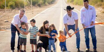 Group of Adults and Children Participate in a Ribbon-cutting on a Rural Road Opening Ceremony with an Orange Ribbon Stretched Across the Road Waist-high. | Ciudadano Seguros