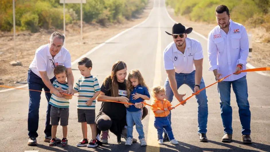 Group of Adults and Children Participate in a Ribbon-cutting on a Rural Road Opening Ceremony with an Orange Ribbon Stretched Across the Road Waist-high. | Ciudadano Seguros