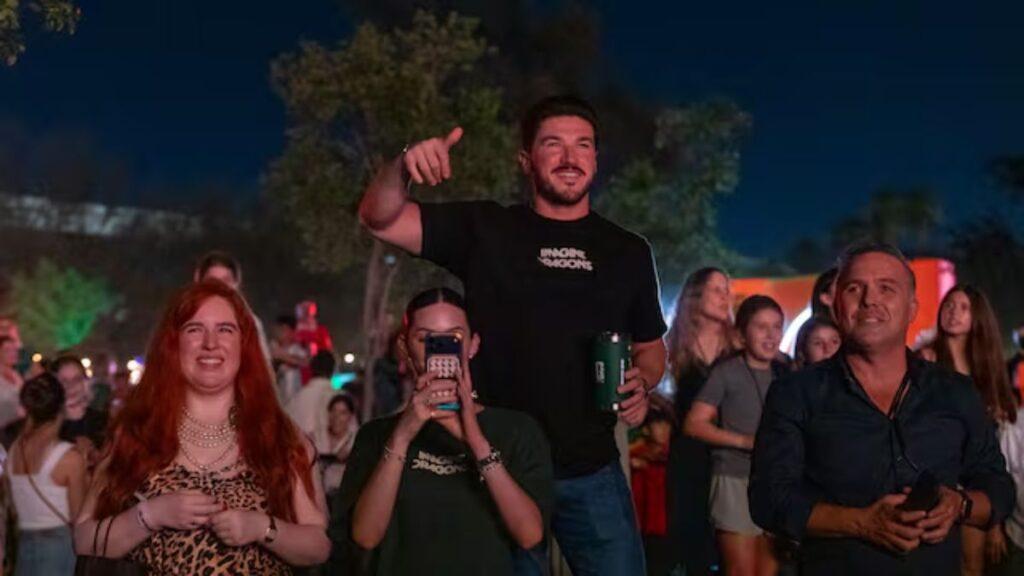 Nighttime Outdoor Crowd with a Man on Someone’s Shoulders Giving a Thumbs-up, Others Smiling and Filming Nearby. | Ciudadano Seguros